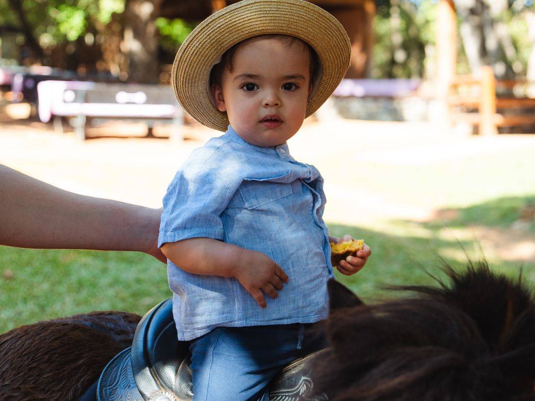 Criança de chapéu de palha montada no cavalo, com sela e estribo
